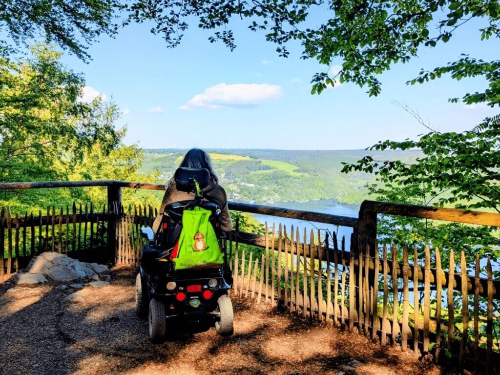 Rollstuhlfahrerin am Aussichtspunkt mit Blick über die Landschaft im Nationalpark Eifel